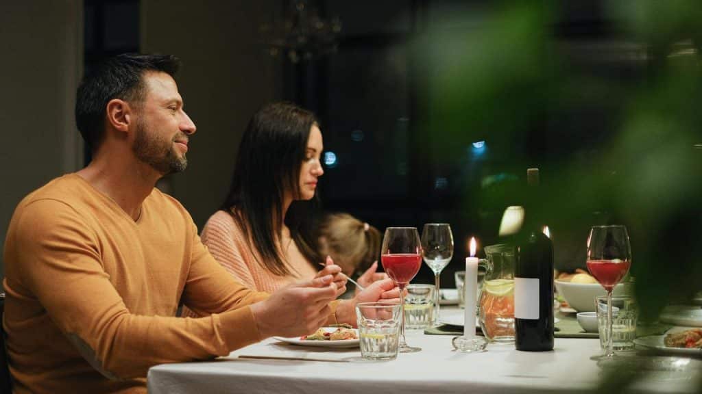 A couple sitting at a candlelit dinner table with wine and food.