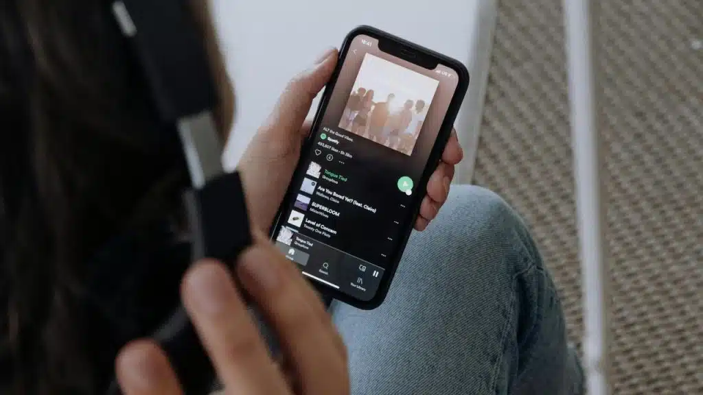 A person holding a smartphone with a music app open while wearing headphones.