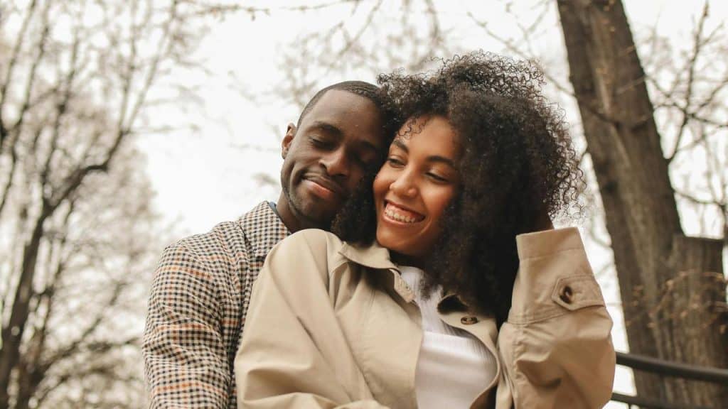 A couple smiling and embracing outdoors among trees.