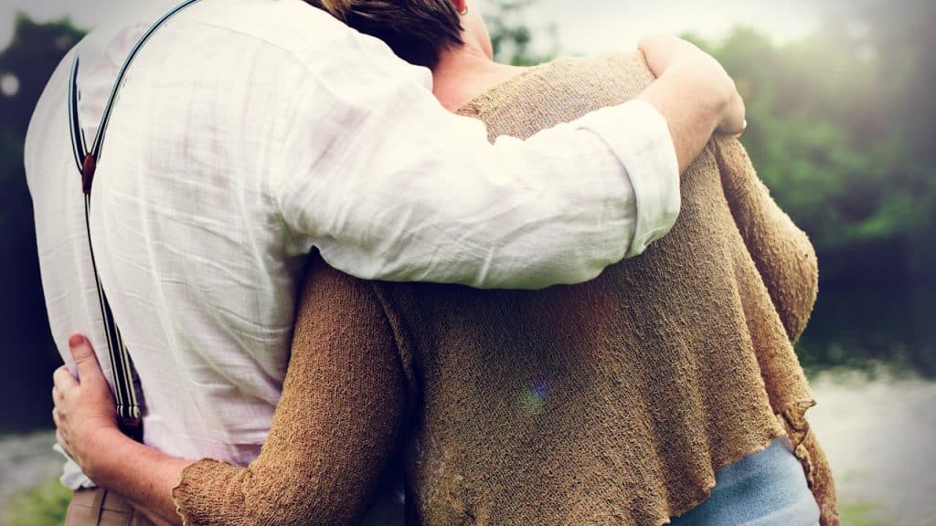 A close-up of a couple embracing outdoors, with the man's arm around the woman's shoulders.