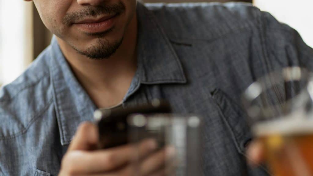 A man holding a smartphone and a glass of beer.