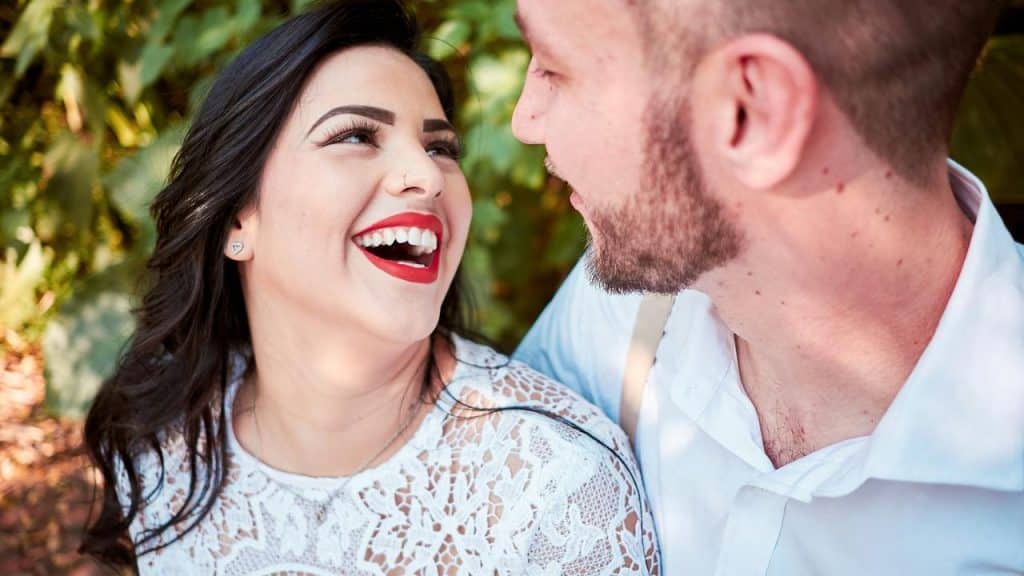 A smiling woman looking at a man while they sit together outdoors.