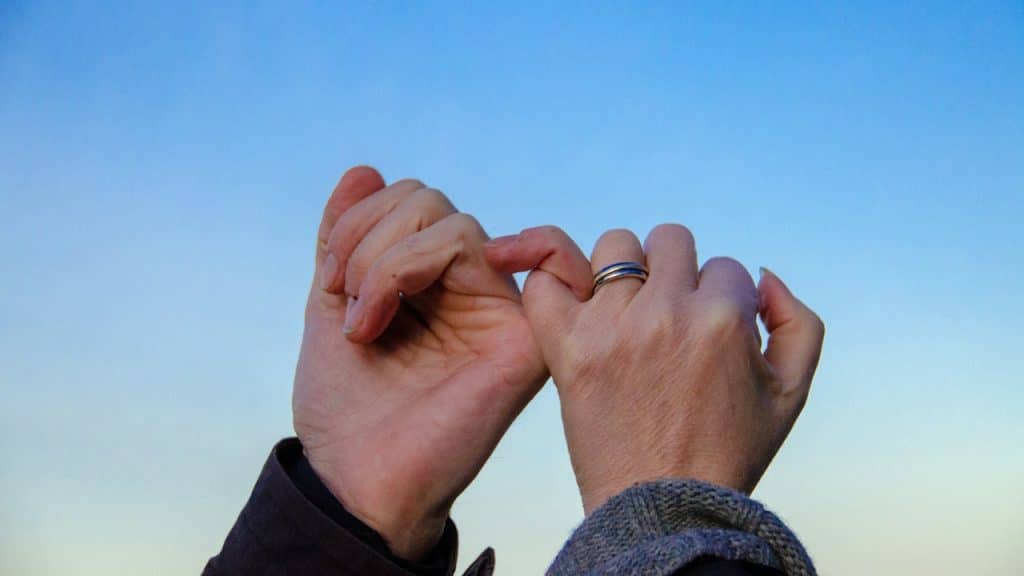 Two hands making a pinky swear gesture, with one hand wearing a silver ring.