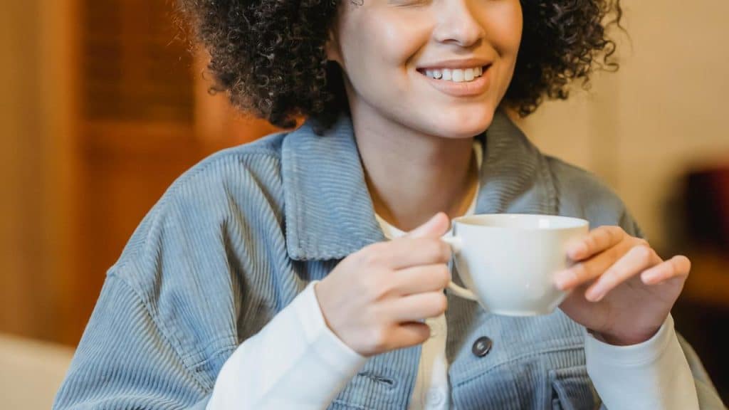 A smiling woman holding a white cup of coffee.