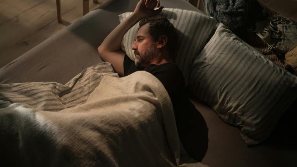 A man sleeping on a couch under a blanket.