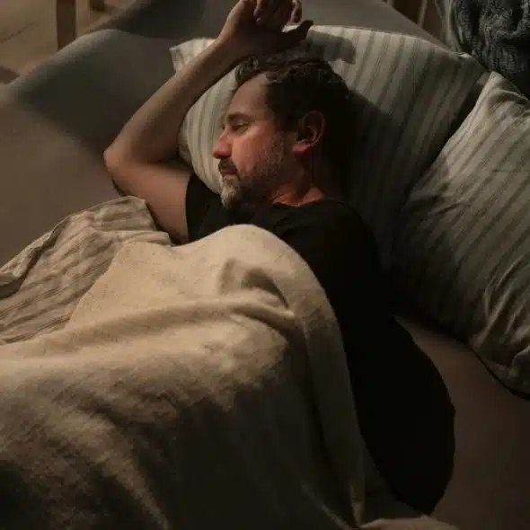 A man sleeping on a couch under a blanket.