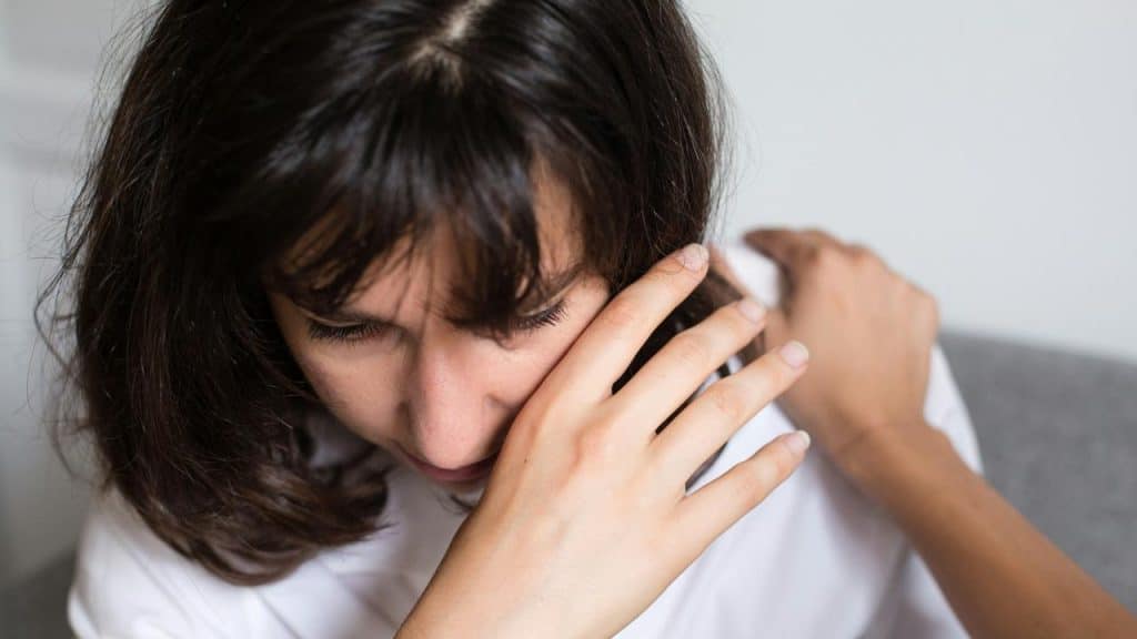 A woman leaning forward with her hand on her face and another hand on her shoulder.
