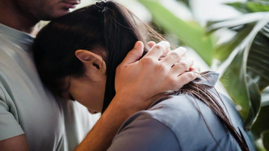 An upset woman being hugged by her husband