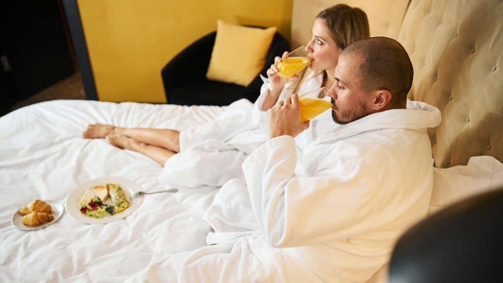 Side view of a newly married couple in bathrobes drinking orange juice.