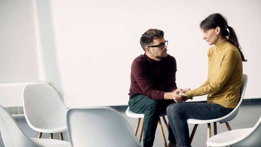 A young couple holding hands while sitting on chairs.