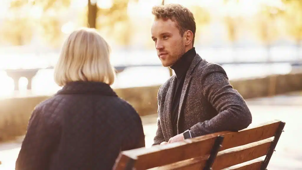 A man listening to a woman while sitting on a bench.