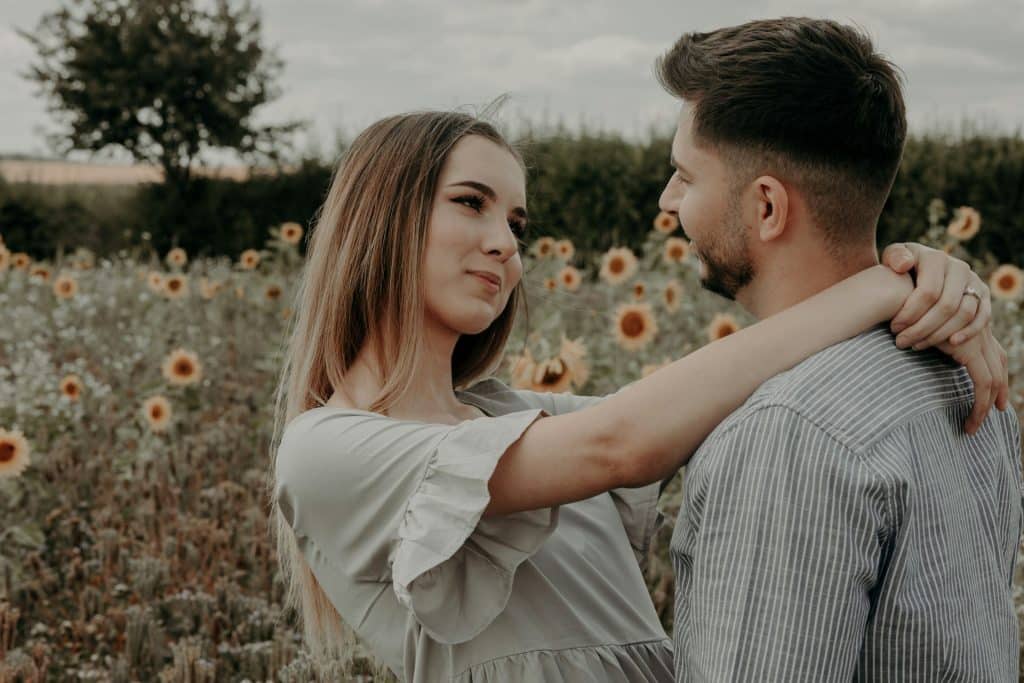 The couple is looking at each other in the middle of a field of flowers.