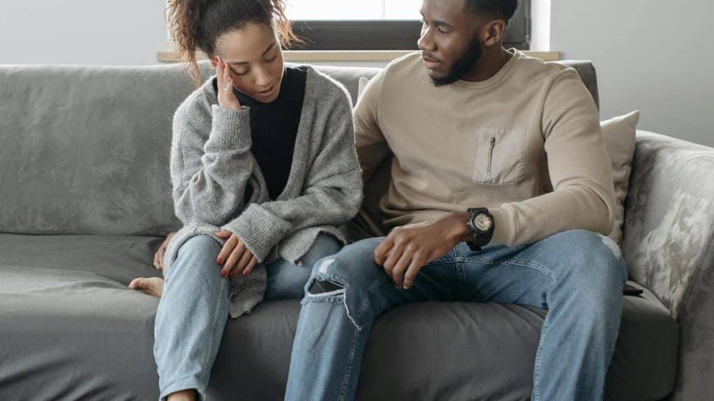 A couple sitting on a couch, with the woman looking upset and the man comforting her.