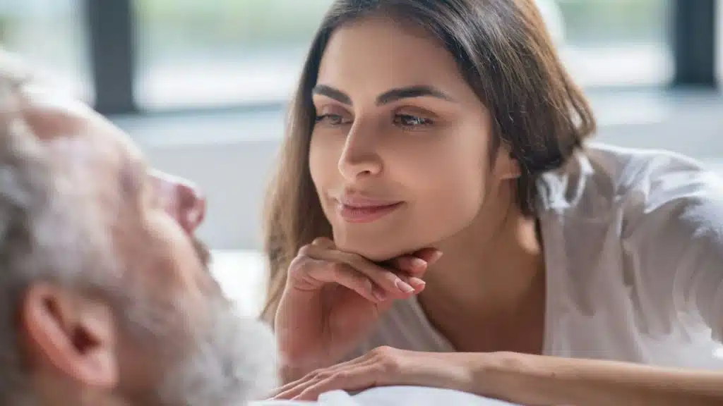A smiling woman is propping her chin on her hand, looking at an older man.