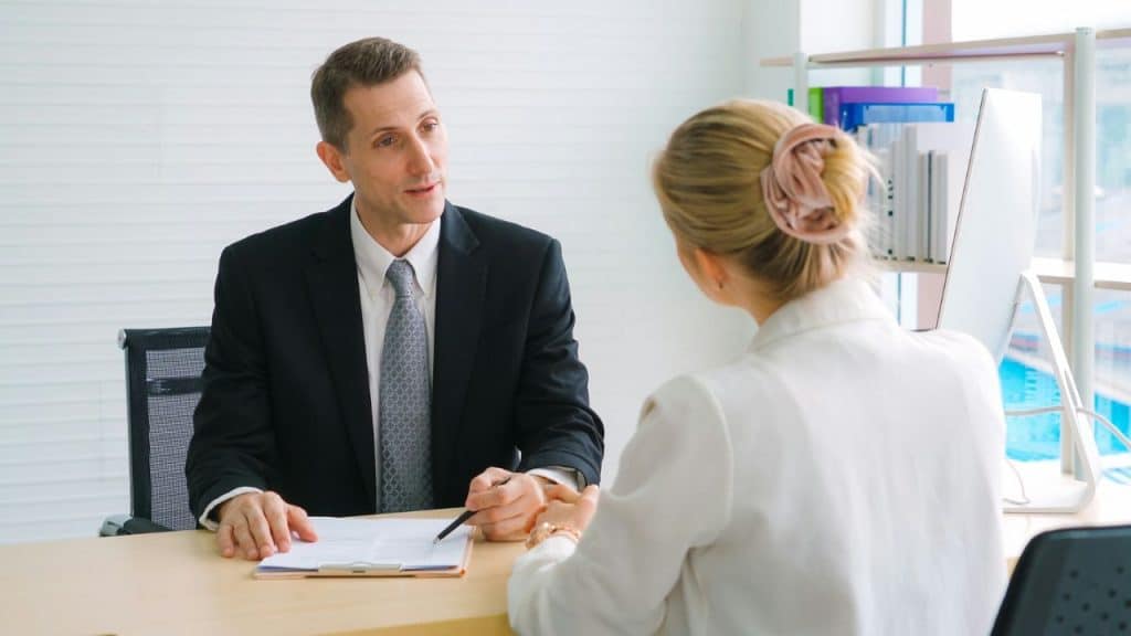 Two professionals in business attire sitting at a desk and discussing paperwork.