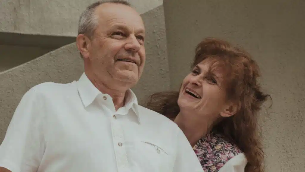 Elderly man in a white shirt and a woman smiling next to him.