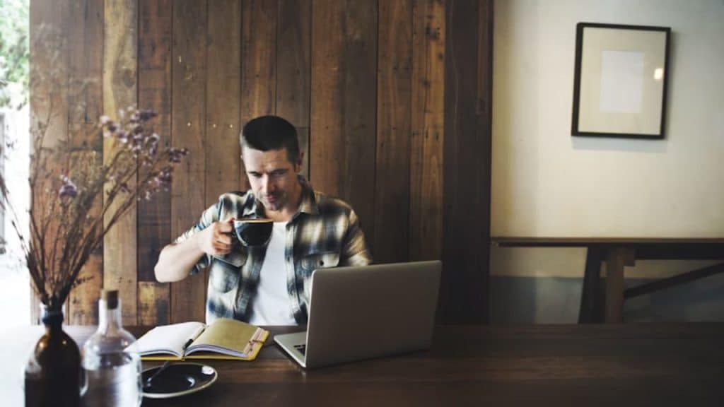 Man reviewing finances with laptop and coffee in a neat home office.