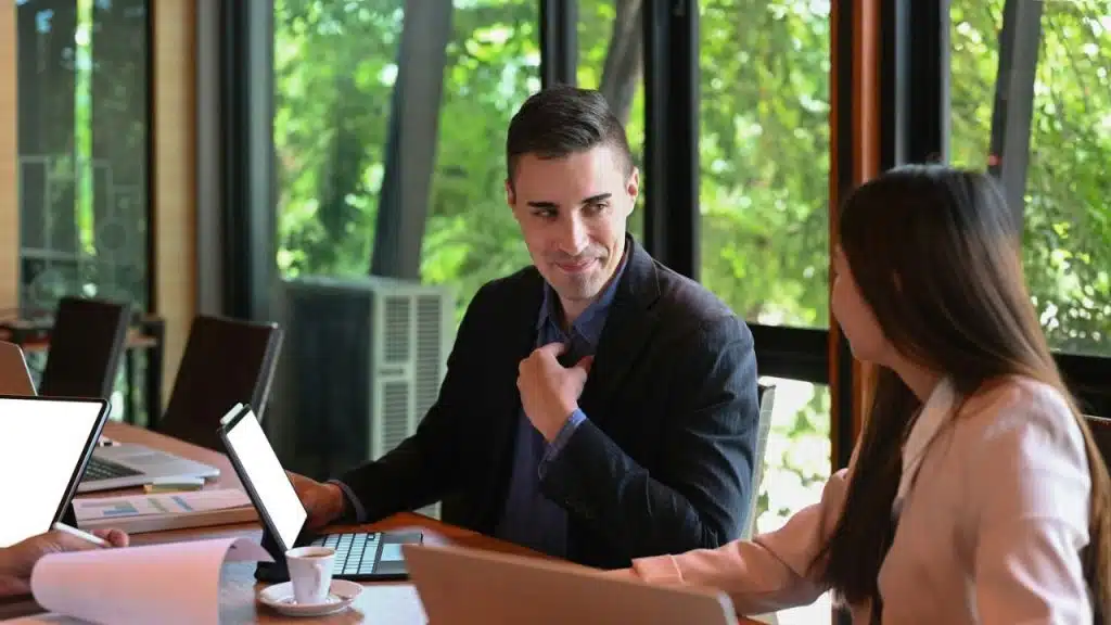 Smiling man in a suit jacket looks at a woman across a table in a bright, green office.