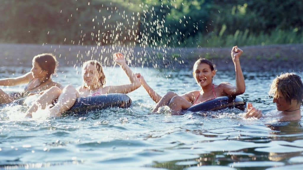 Four smiling people splashing water while floating on inner tubes in a lake.