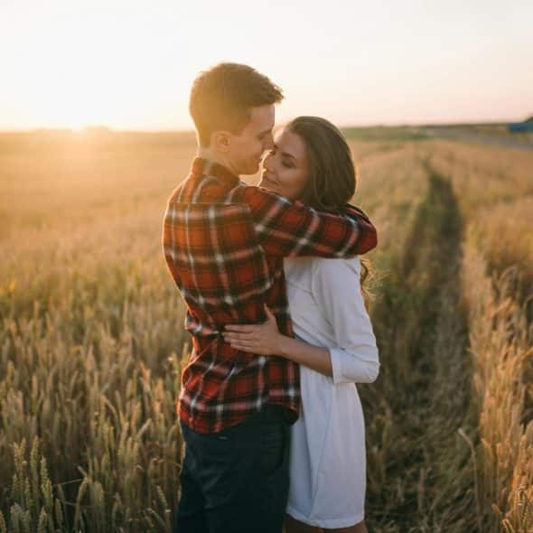 The couple is hugging and smiling on the field.