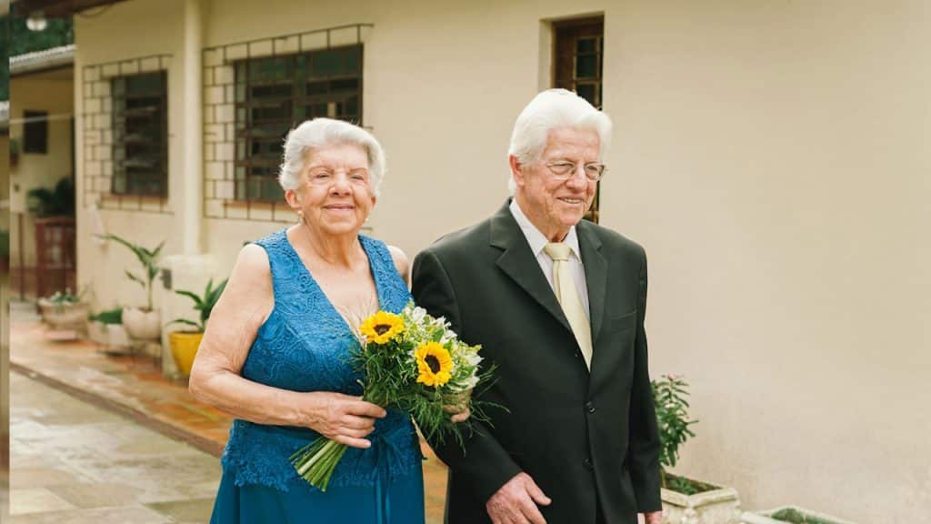 An old man and a woman holding flowers standing next to each other