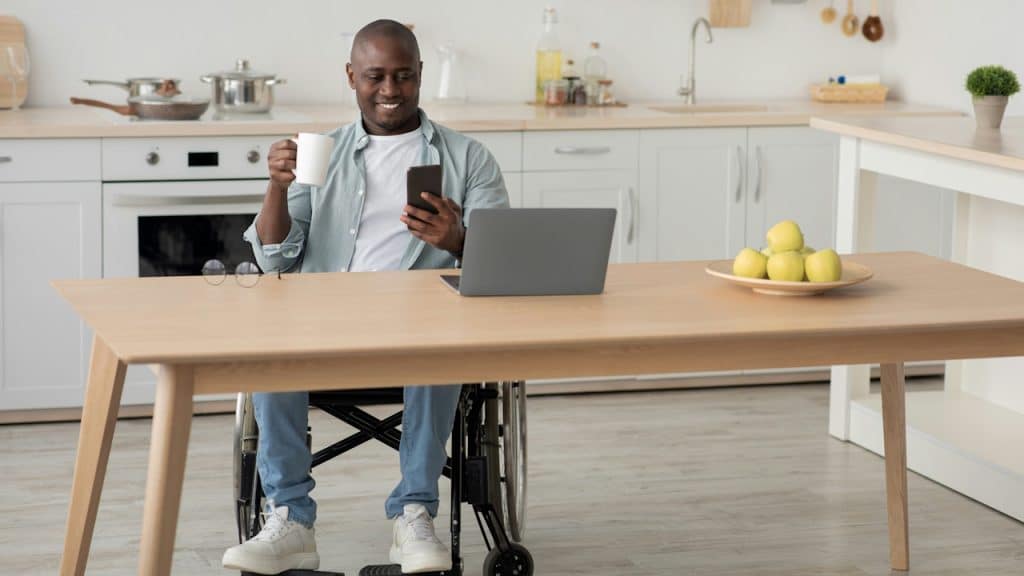 A smiling man sitting at a table and having coffee while using his phone.