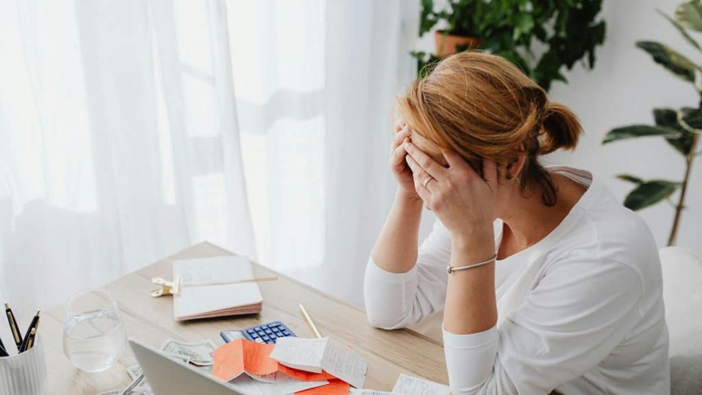 A woman sitting at a desk with her head in her hands looking stressed.