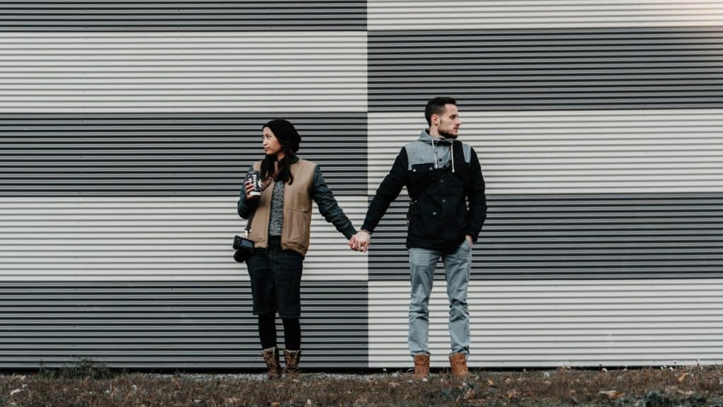 A couple standing and holding hands while looking in opposite directions.