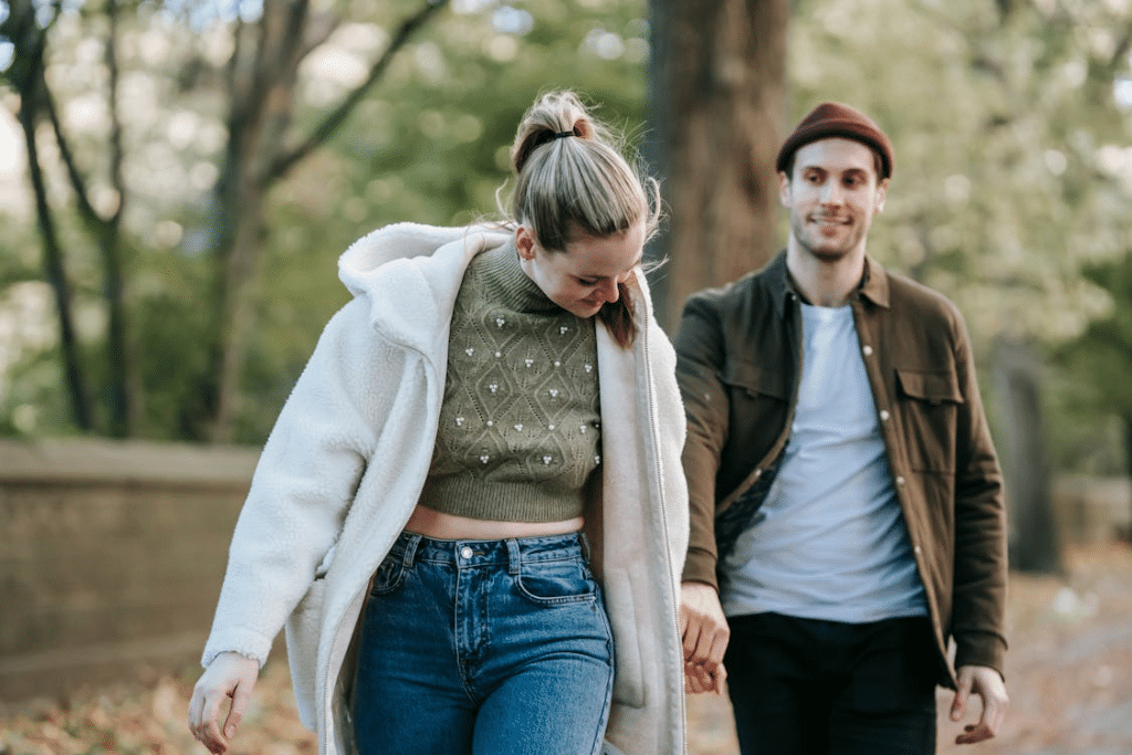 Happy young guy following girlfriend in autumn park