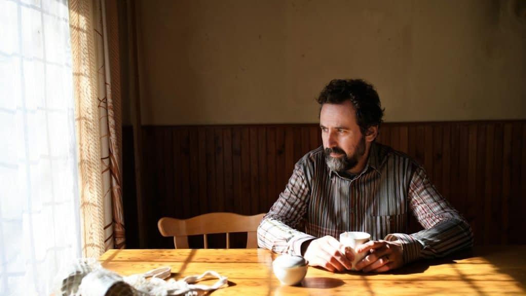 An unhappy man having coffee while sitting at a table indoors.