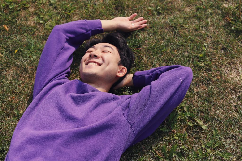 The smiling man is lying on the ground with his hands behind his head.