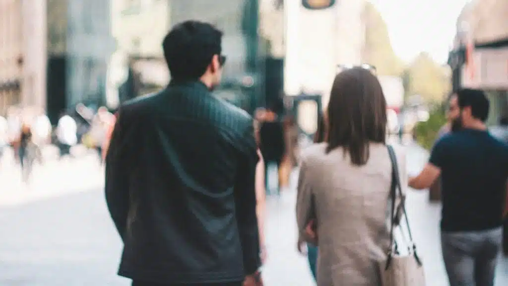 A blurry photo of a man and a woman walking away from the camera on a city street.