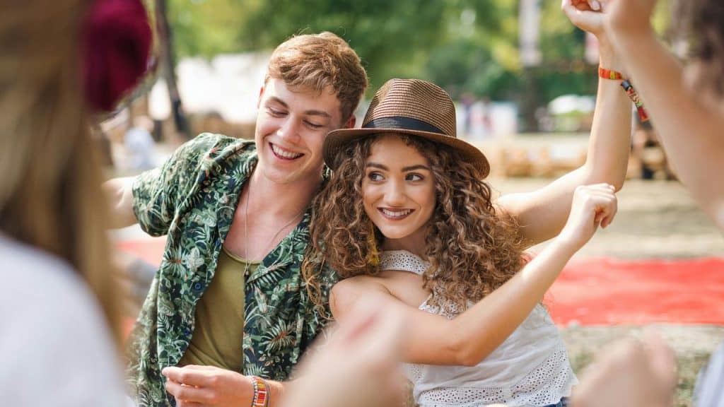 A young couple smiling and dancing together outdoors at a summer festival.