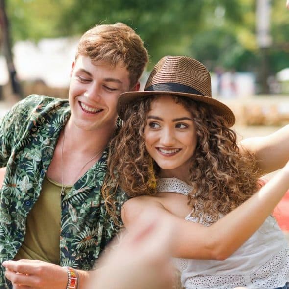 A young couple smiling and dancing together outdoors at a summer festival.