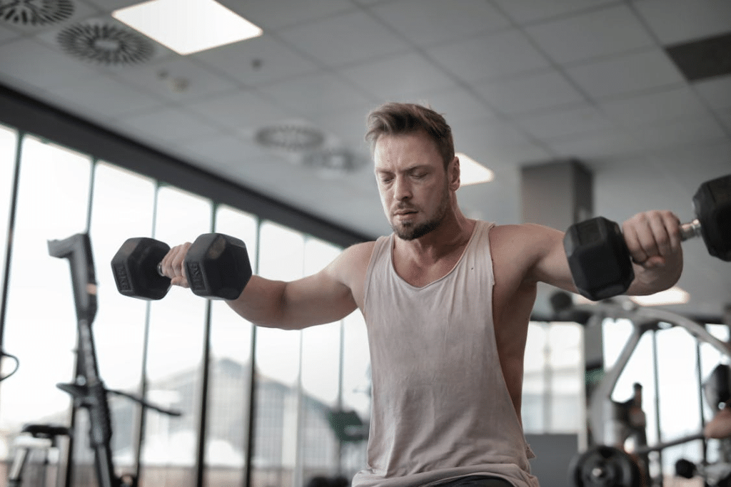 Man in Gray Tank Top Holding Black Dumbbells