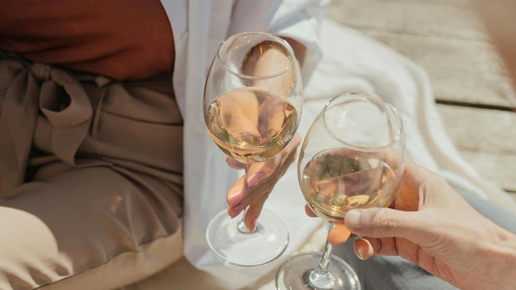 A close-up of two people clinking glasses of white wine.