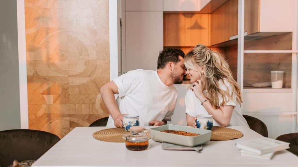 A couple leaning close together and smiling at a table with food and coffee.