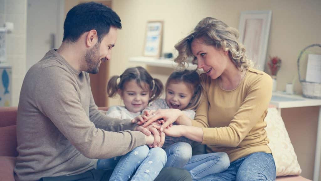 A couple holding hands with their daughters in their living room.