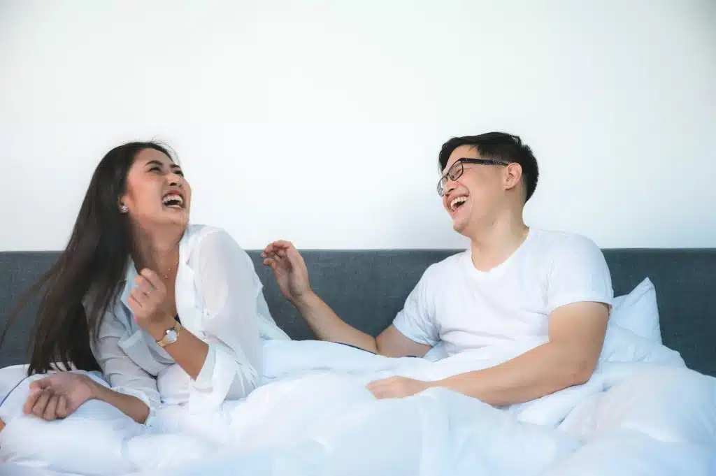 The couple is laughing together on the bed.