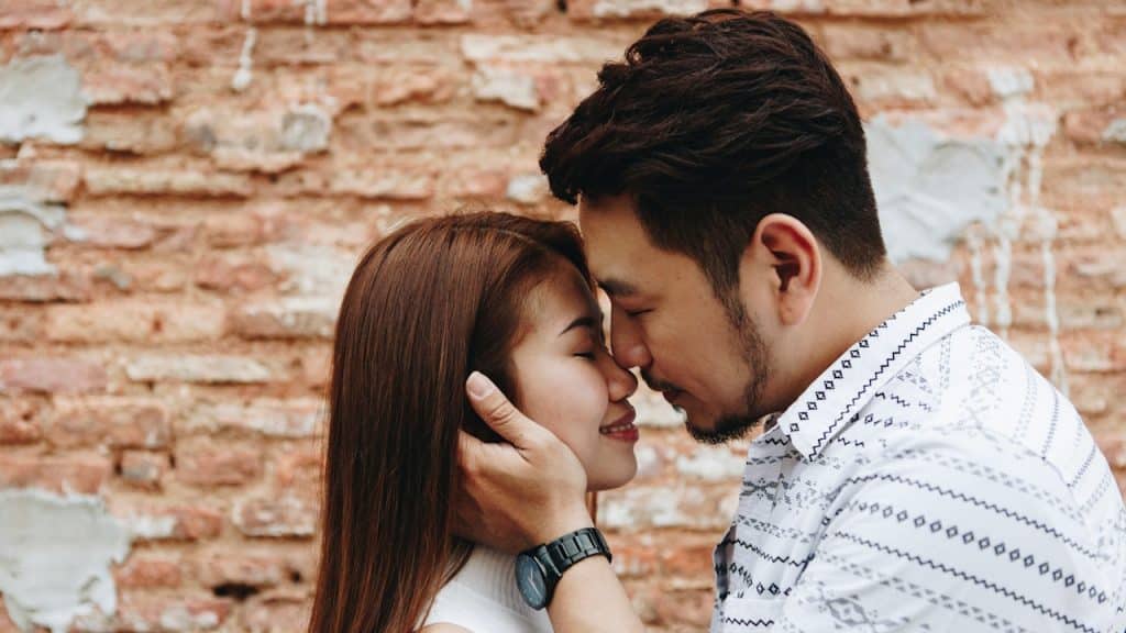 A couple stands face-to-face with their foreheads touching and eyes closed.
