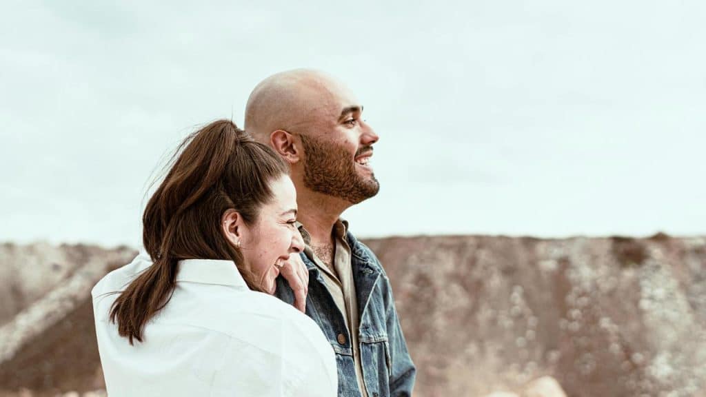 A smiling couple embracing outdoors near rocky hills.