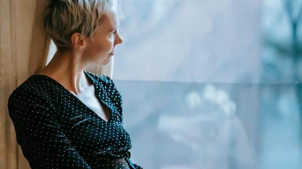 A woman with short blonde hair gazing out of a window.