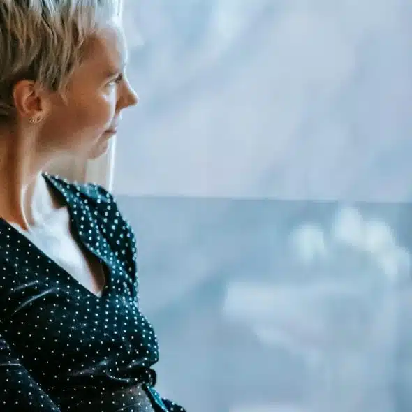 A woman with short blonde hair gazing out of a window.