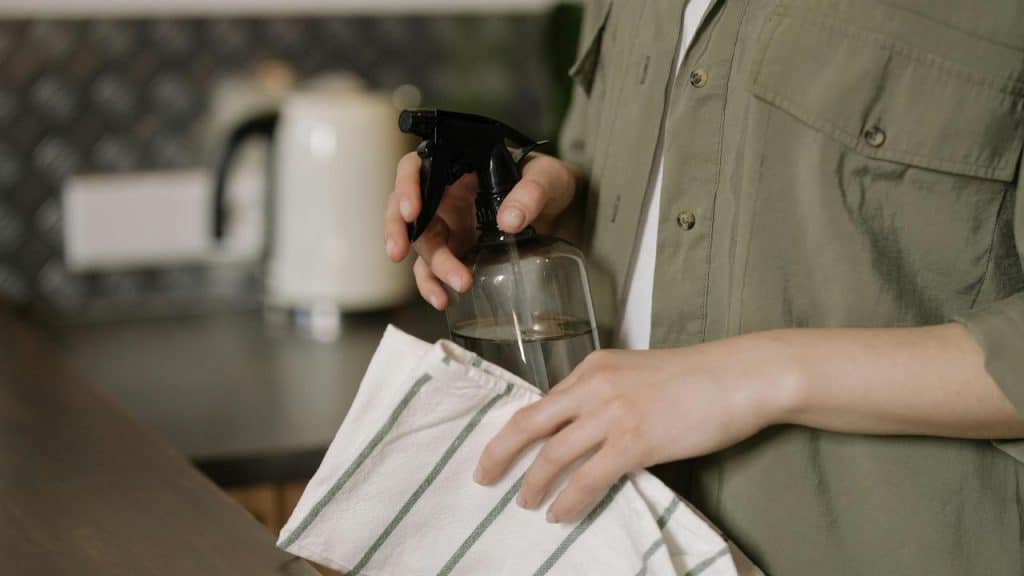 A person holding a spray bottle and cleaning cloth in a kitchen.