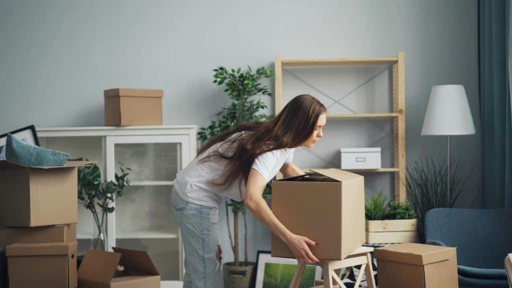 A woman packing cardboard boxes in a room filled with moving supplies.