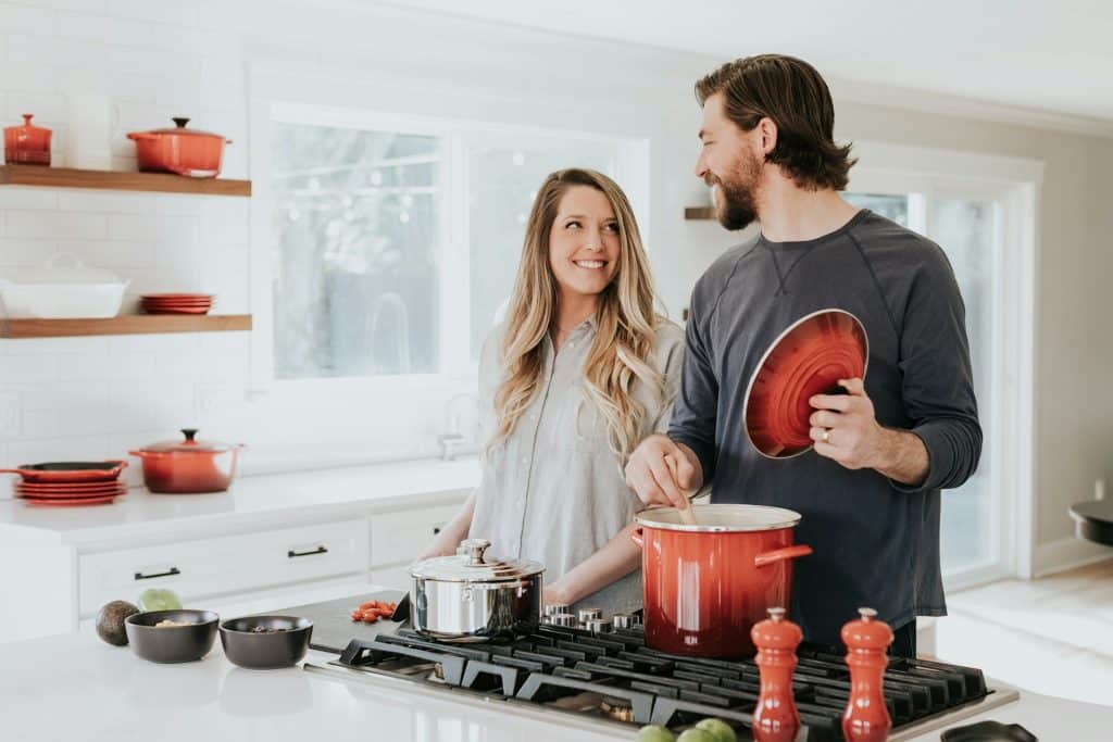 The man and the woman are looking at each other while cooking in the kitchen.