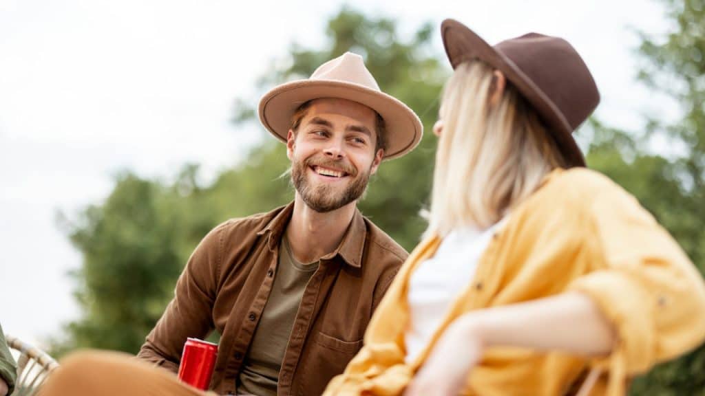 A couple in hats smiling at each other outdoors.