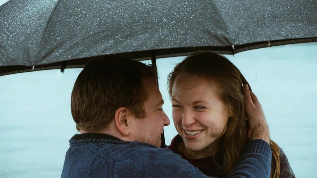 A couple smiling under an umbrella in the rain.