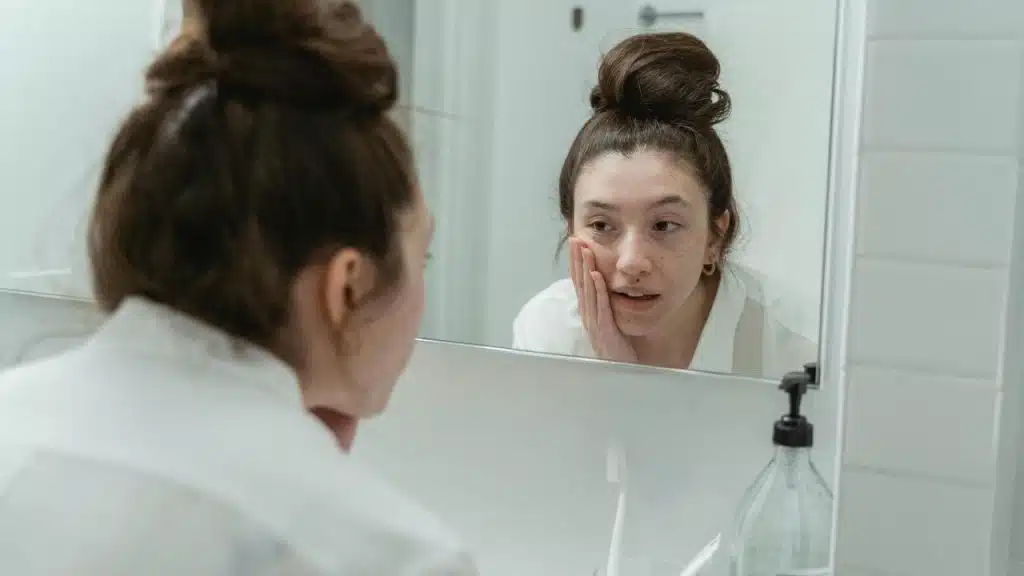 A young woman looks at herself in a bathroom mirror.