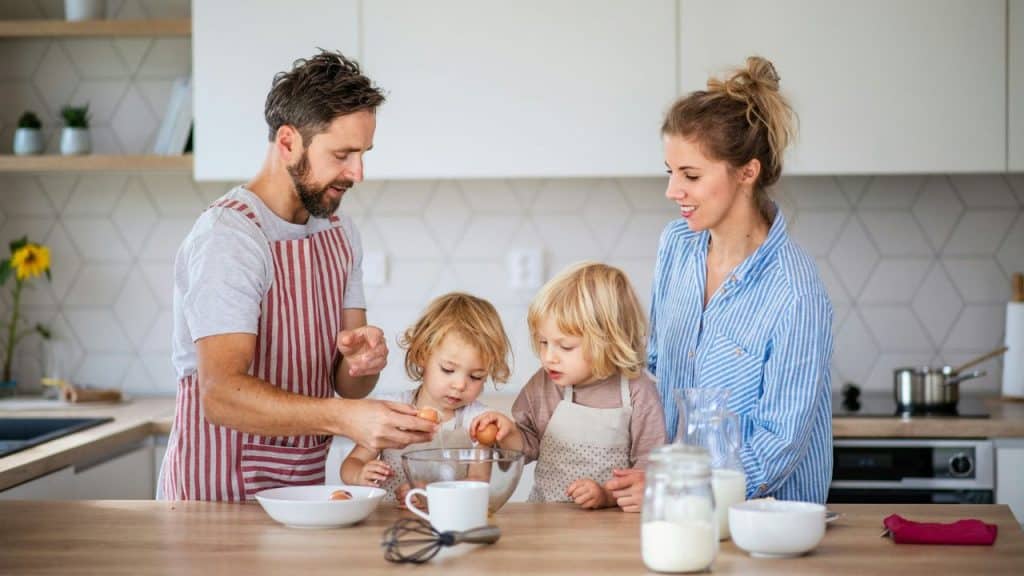 Parents and two small children in a kitchen cooking with eggs and a bowl.